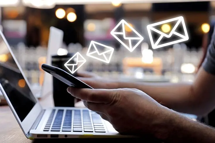 Person using a smartphone and laptop with floating email icons, representing email marketing, digital communication, and online customer engagement.